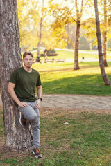 A portrait of a friendly young guy in a park by the tree	