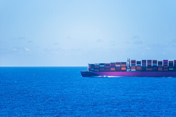 Large cargo container ship fully loaded with colorful containers is sailing through the ocean. 
