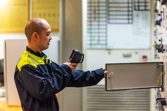 The marine engineer officer uses a thermal camera to inspect electrical equipment, carefully checking for overheating in switch contacts to ensure operational safety and reliability.