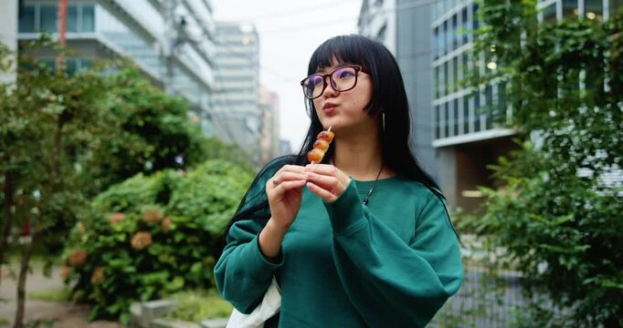 Japanese woman, street food and eating snack outdoor on vacation, holiday or travel for culture. Asian girl, dessert and sweets in city with grilled dango or hungry for traditional skewered dumplings