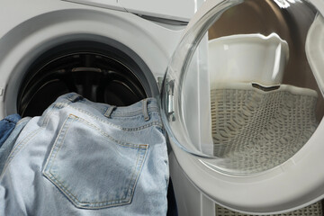 Washing machine with dirty jeans and other denim clothes indoors, closeup