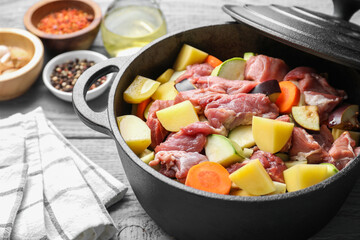 Cooking stew. Uncooked meat and vegetables in pot on light grey wooden table, closeup