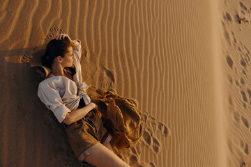 Lonely woman laying on top of a sandy dune, gazing into the distance under the open sky