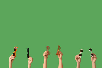 Female hands with different stylish sunglasses on green background