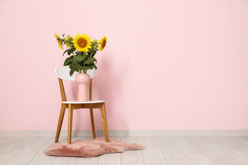 Vase with beautiful sunflowers on chair near pink wall in living room
