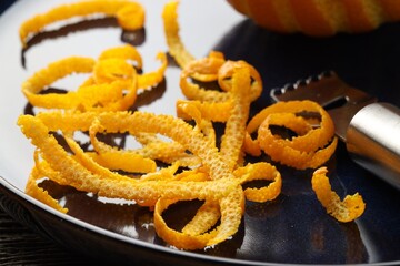 Plate with fresh orange zest and zester on table, closeup