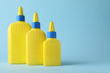 Bottles of glue on light blue background, space for text