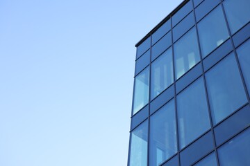 Exterior of modern building with many windows against light blue sky, low angle view. Space for text