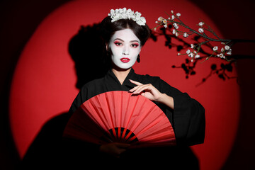 Beautiful young geisha with fan on red background