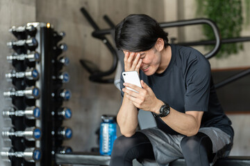 ジム・フィットネスジムでスマホで調べる・検索する体調不良の若いアジア人男性
