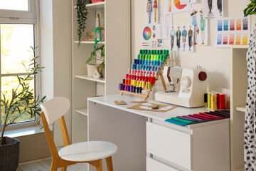 Fototapeta premium Sewing machine with patterns and thread spools on tailor's table in atelier