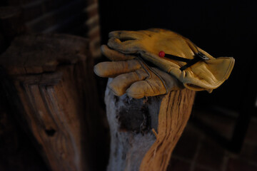 A worn yellow work glove resting on a wooden stump near a fireplace, suggesting preparation for a cozy evening of wood handling or fire-making in a rustic cabin