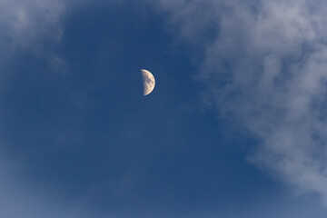 The moon in the dark blue sky with white clouds, closeup