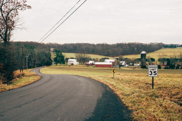 Country road curving through lush farmland with a speed limit sign on a quiet day in rural...