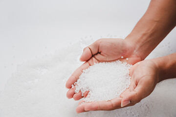 Hands hold clear white plastic pellets, raw materials for various manufacturing processes. These pellets are widely used in industries to produce products like packaging, bottles, and equipment parts.