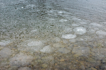 Ice forming on a calm lake surface in winter, showing distinct patches and clear waters beneath, captured during a chilly afternoon in a serene natural setting