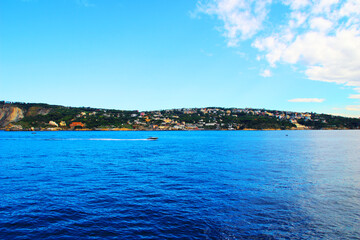 Splendid panorama from the Gulf of Naples with a monochrome speedboat surfing on the blue, wavy waters of the Tyrrhenian Sea becoming iridescent on the right with green rocky coast in the back