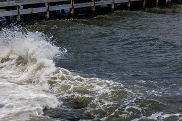 The waves crash vigorously against the wooden pier, sending splashes of water into the air. A...