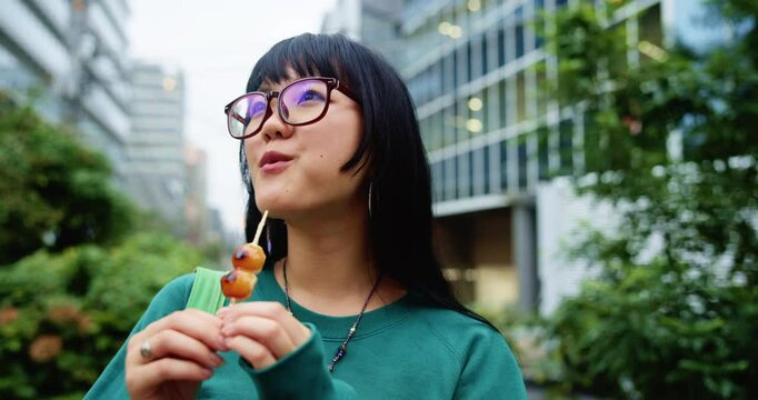 Japanese woman, street food and eating sweets outdoor on vacation, travel or thinking on holiday. Asian girl, dessert and snack in city with grilled dango or hungry for traditional skewered dumplings