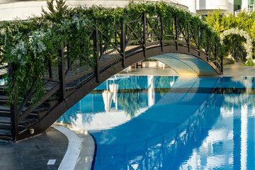 Wooden bridge decorated with green plants over the pool in a summer holiday hotel