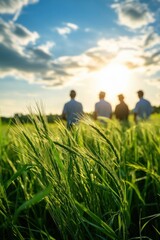 Four silhouettes stand in a sunlit field, surrounded by lush green grass and a beautiful sky filled with clouds.