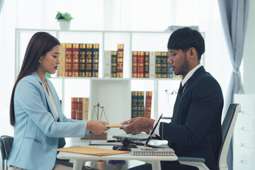 Fototapeta premium Legal Counsel: A professional female lawyer hands over a document to her male colleague in a modern office setting.