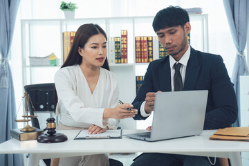 Legal Counsel Collaboration: Two Asian lawyers, a man and a woman, work together on a laptop in a modern law office.  They are reviewing documents and engaging in a serious discussion.