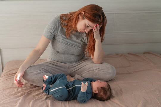 A Caucasian woman sits on a bed next to a crying baby. Postpartum depression.