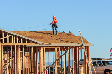 A construction worker atop the structure of a home under construction in a new subdivision, wearing...