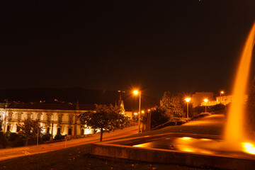 Paisagem noturna de uma fonte de um parque, uma estrada e alguns edificios.