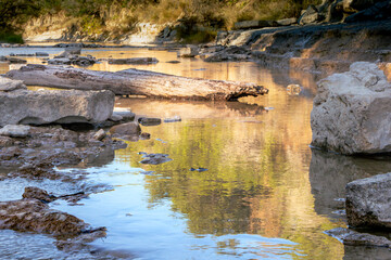 A tranquil stream gently flows through Dinosaur Valley State Park in Glen Rose, TX, reflecting lush greenery and bathed in soft sunlight. 