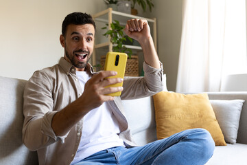 Man using phone celebrating victory, successful achievement with fist up in the air. Arm raised.