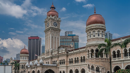 An old Sultan Abdul Samad Building in Kuala Lumpur. A clock tower with domes and spires against the blue sky. The brickwork of the walls, galleries, arches,columns are visible. Malaysia.Merdeka Square