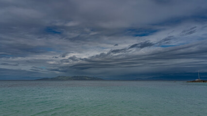 Beautiful seascape. Turquoise calm ocean to the horizon. Mountains in the distance, against the blue sky and clouds. The silhouette of a yacht with a high mast. Madagascar. Nosy Tanikeli   