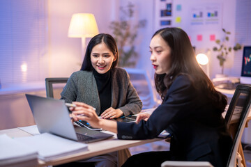 Two women are sitting at a desk with a laptop open in front of them