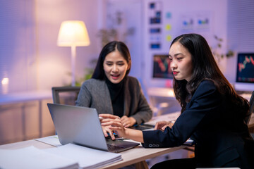 Two women are sitting at a desk with a laptop in front of them