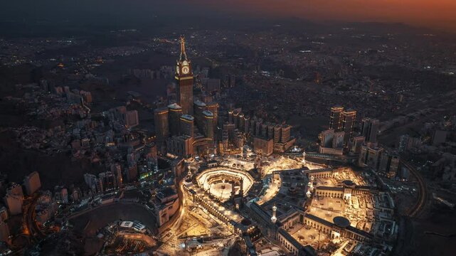 Aerial hyperlapse view at night of the illuminated Grand Mosque and Abraj Al-Bait Clock Tower in Mecca, showcasing the city&rsquo;s vibrant glow as lights shimmer across the holy site