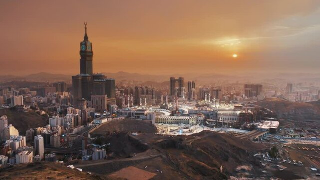 A breathtaking sunrise illuminating the Abraj Al-Bait Clock Tower and Grand Mosque in Mecca, surrounded by the sprawling city and mountains in a serene morning view
