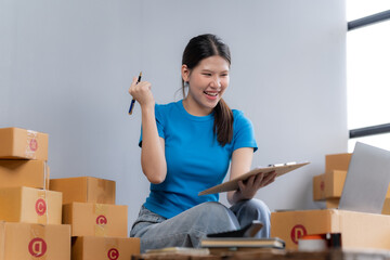 Online Business Success: A young, enthusiastic Asian woman celebrates her e-commerce success,...