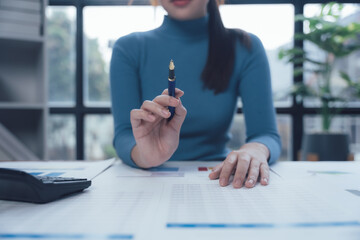 Strategic Planning: A businesswoman's hand holding a pen, poised over important financial...