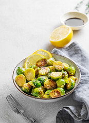 Fried brussels sprouts in a bowl with soy or balsamic sauce, lemon and sesame on a light background with fork and napkin.