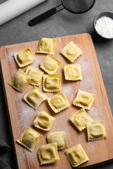 Fototapeta premium Homemade pasta ravioli on wooden cutting board on dark background with flour and rolling pin.