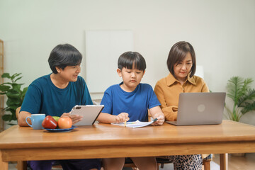 Asian parents and their children sit together at the table in the morning, studying online using tablets and computers, fostering a productive and focused family learning environment