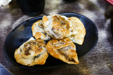 close up of Chinese pan fried dumplings with meat and vegetables stuffed filling on a black plate
