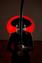 A woman in a mask and Japanese traditional headdress sugegasa poses with a samurai sword. Japanese...