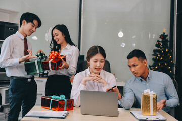 full length view of a group of business team wearing red Santa hat and exchange gift box together in the office for Christmas.