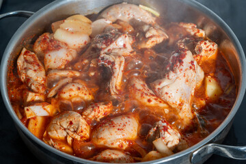 A spicy Korean chicken stew with potatoes, onions, and red chili-based sauce boiling in a pot.