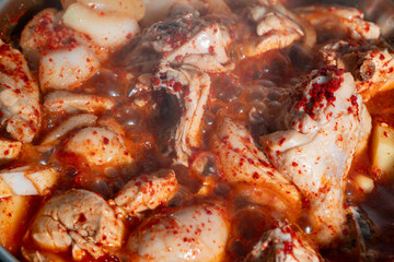 A spicy Korean chicken stew with potatoes, onions, and red chili-based sauce boiling in a pot.