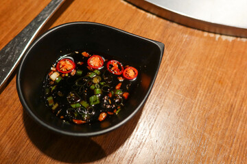 close up of spicy chilli pepper spring onion soy sauce in a black dish for dipping hot pot with copy space