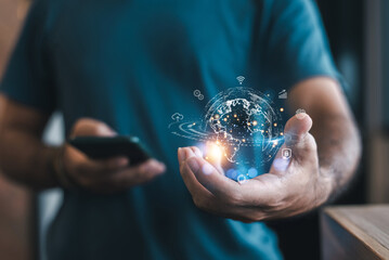 A man holding a glowing digital globe in his hand, symbolizing global connectivity and technology, while using a smartphone.